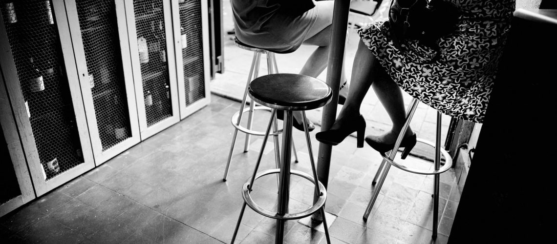 KMK21G Dos mujeres jovenes irreconocibles tomando una copa de vino en un bar sentadas en un taburete. Barcelona, Catalonia, Spain.